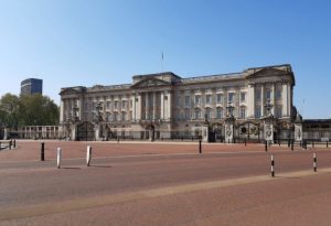 a small clock tower in the middle of a road with Buckingham Palace in the background