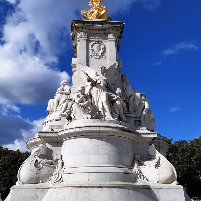 a statue of a person with Victoria Memorial, London in the background