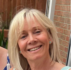 Smiling woman with blonde hair and a brick wall background.